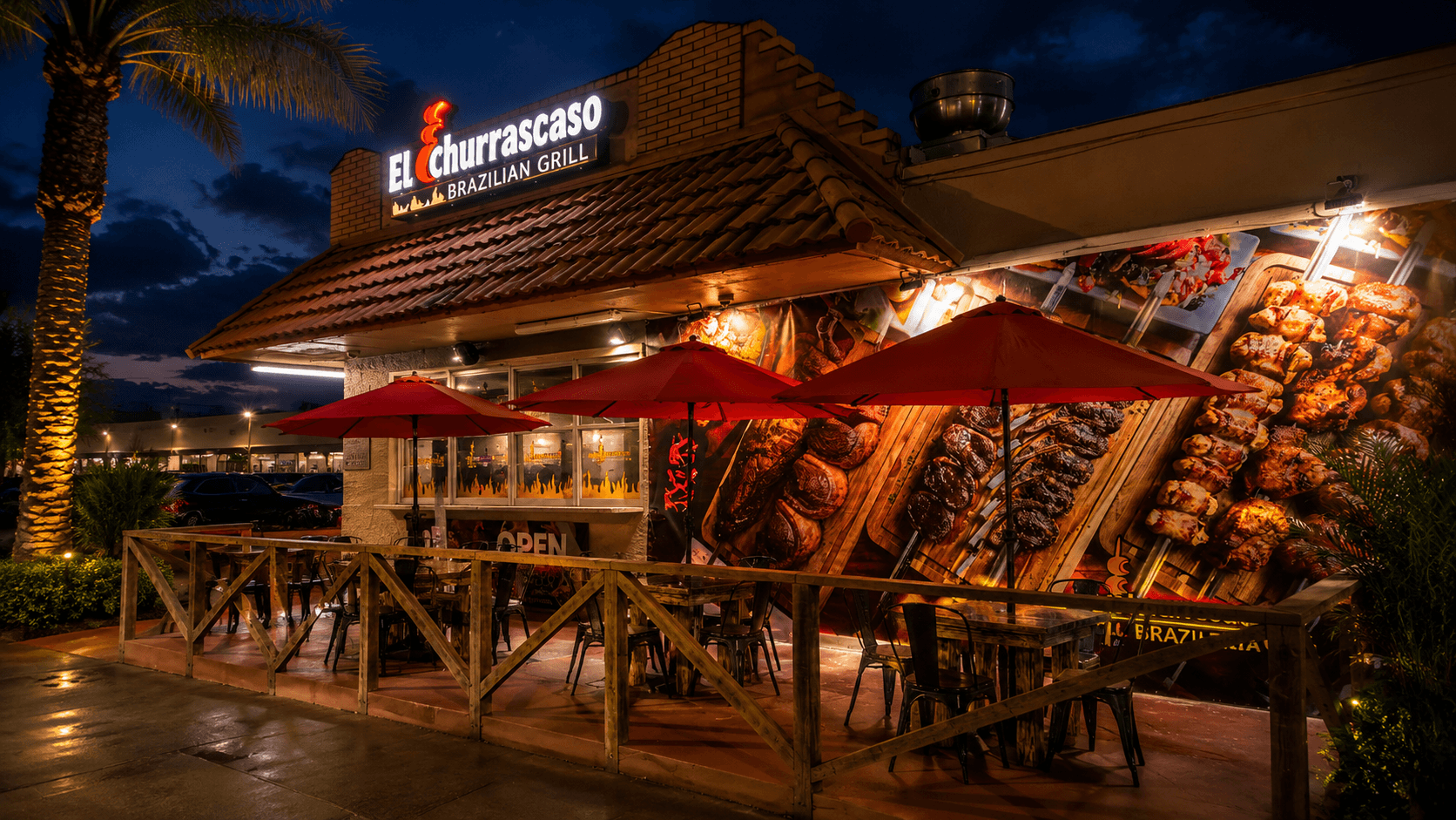 El Churrascaso Brazilian Grill exterior at dusk with illuminated channel-letter signage, red patio umbrellas and a large grilled-meats wall mural