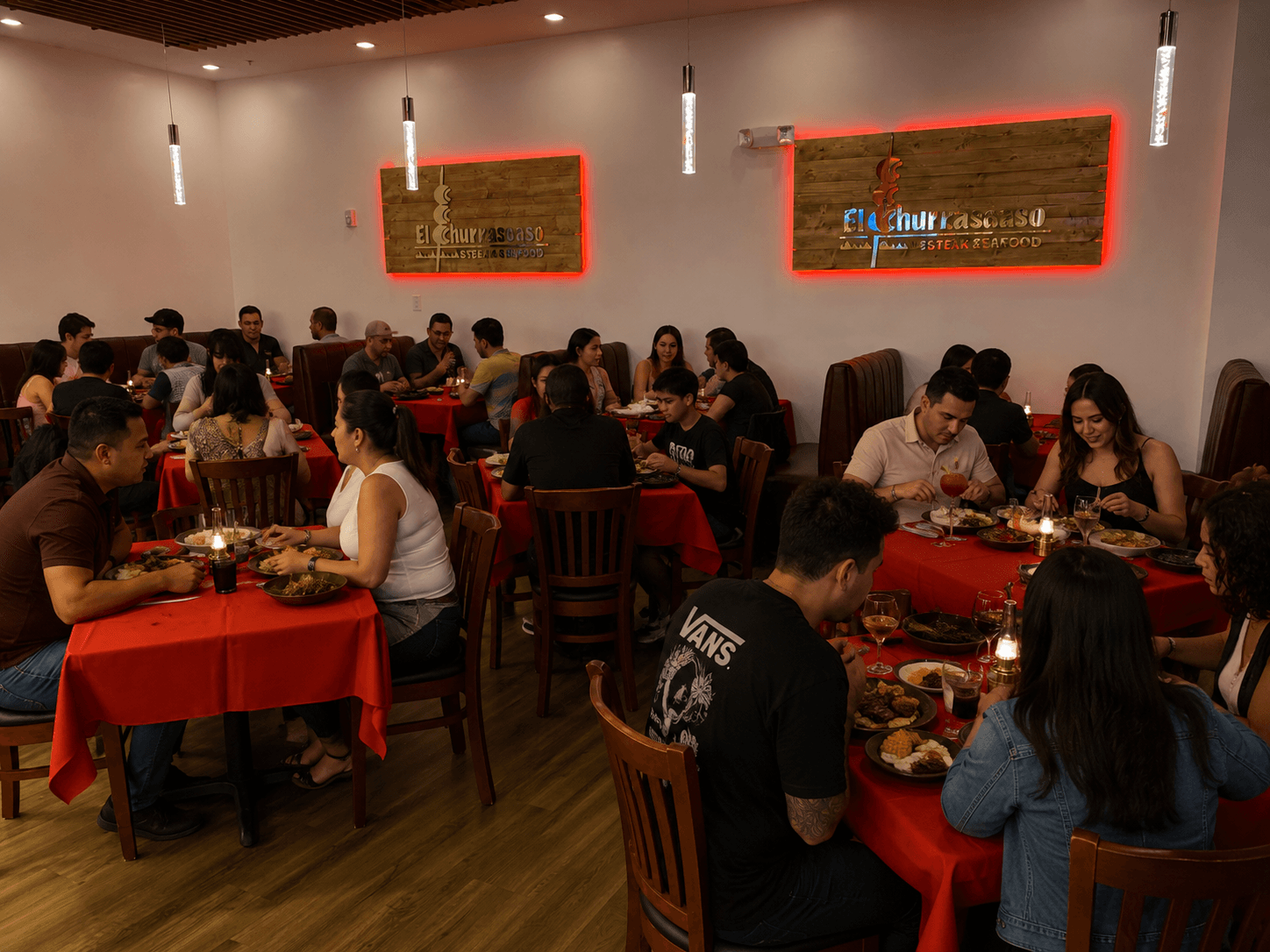 Busy El Churrascaso dining room with guests at red-clothed tables beneath two red-halo illuminated wood-backed acrylic signs