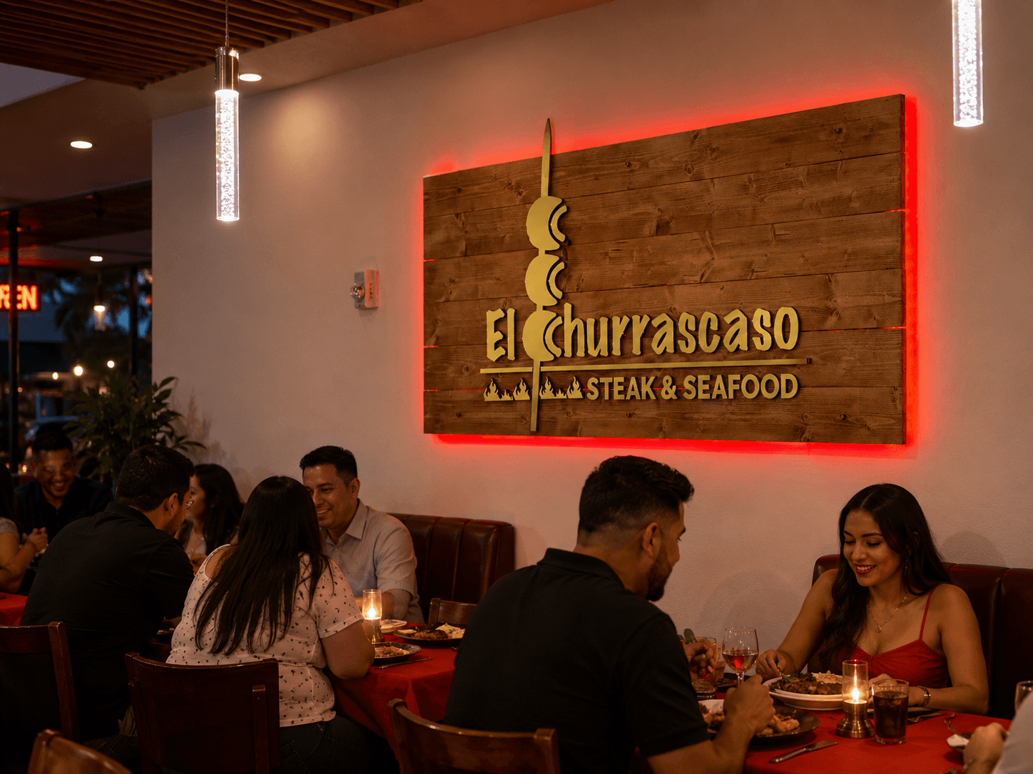 Guests dining beside a large wood-backed gold El Churrascaso Steak & Seafood acrylic sign with a red halo glow